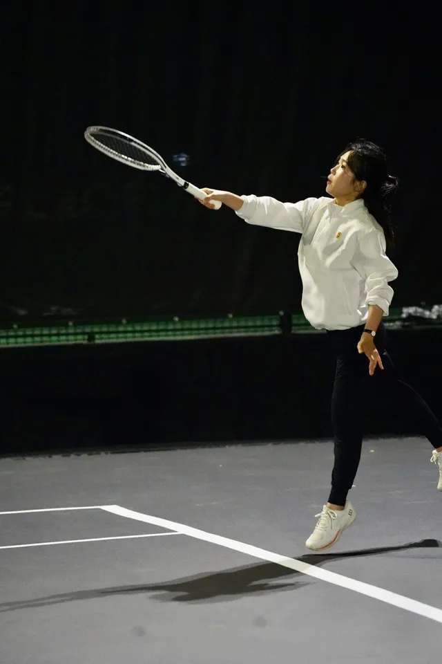 Jiyae reaching for a volley on an indoor tennis court